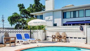 Zona de piscina con sillones de descanso y una sombrilla blanca.