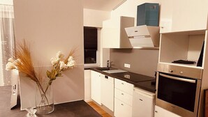 Eine moderne Küche mit weißen Schränken, einer schwarzen Arbeitsplatte und Edelstahlgeräten, darunter ein Geschirrspüler und ein Backofen.