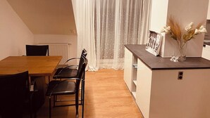 Eine kleine Küche mit Holztisch und -stühlen, einer Arbeitsplatte und einem Fenster mit leichtem Vorhang.