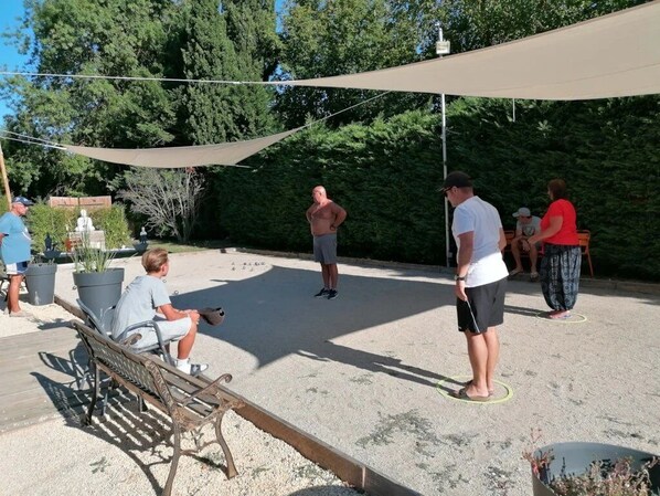 Un espacio al aire libre con una zona de estar con sombra, un banco y un grupo de personas.