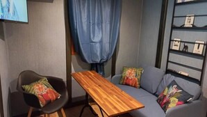 Una habitación con una mesa de madera, un sofá gris, una silla negra con un cojín de tigre y una cortina azul.