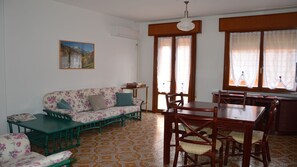 A room with a sofa, a dining table with chairs, a small table with a box, and a painting on the wall. - Bright house near the beach in Caorle (Caorle)