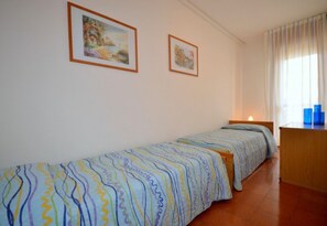 Ein Zimmer mit zwei Betten, einem fensterbelagten Fenster und zwei gerahmten Bildern an der Wand.