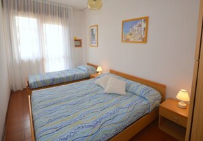 Un dormitorio con una cama grande, una cama más pequeña, una mesita de noche, una lámpara y un cuadro en la pared.