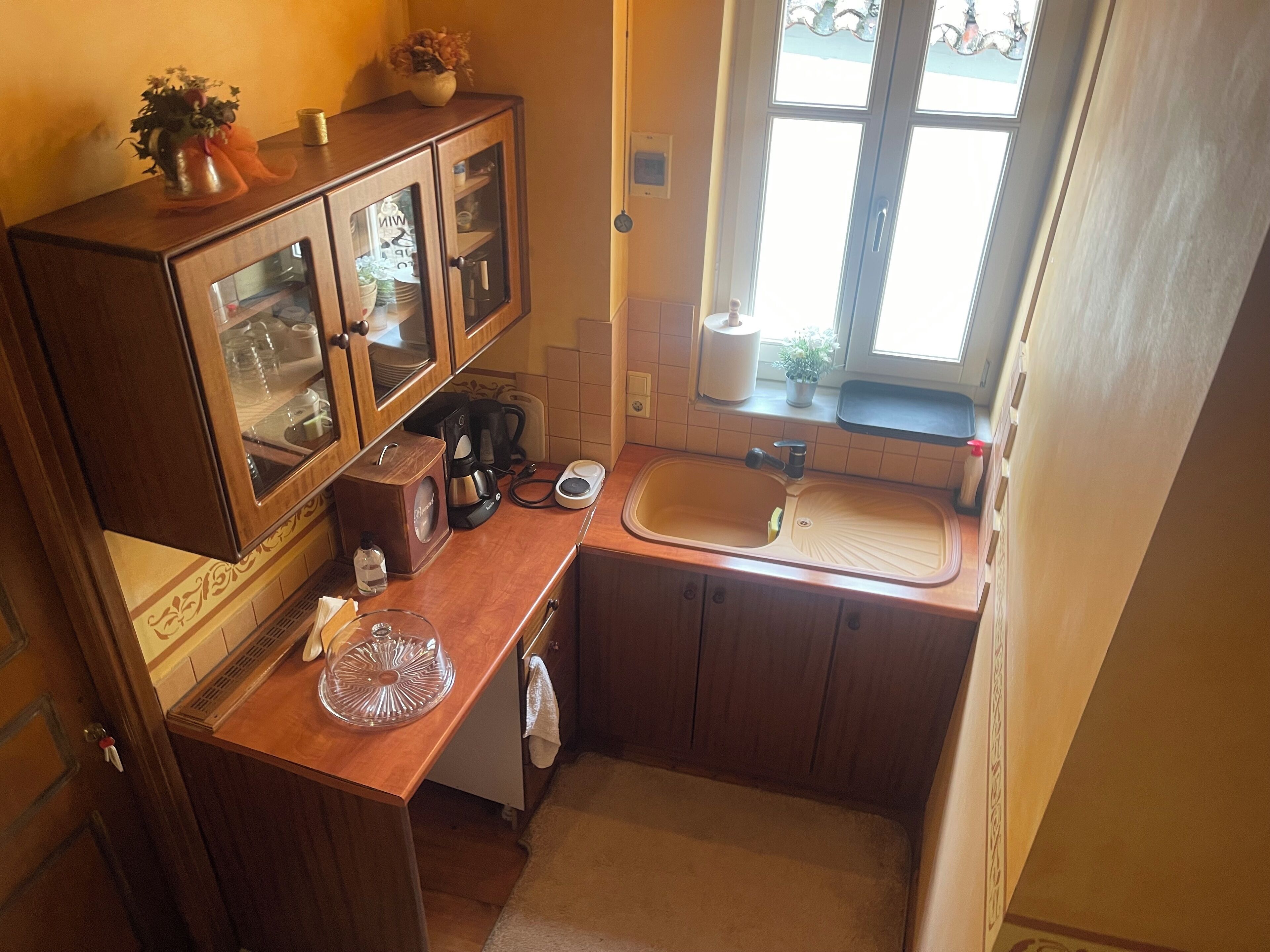 A compact kitchen with a sink, a coffee maker, and a cabinet with glass doors.