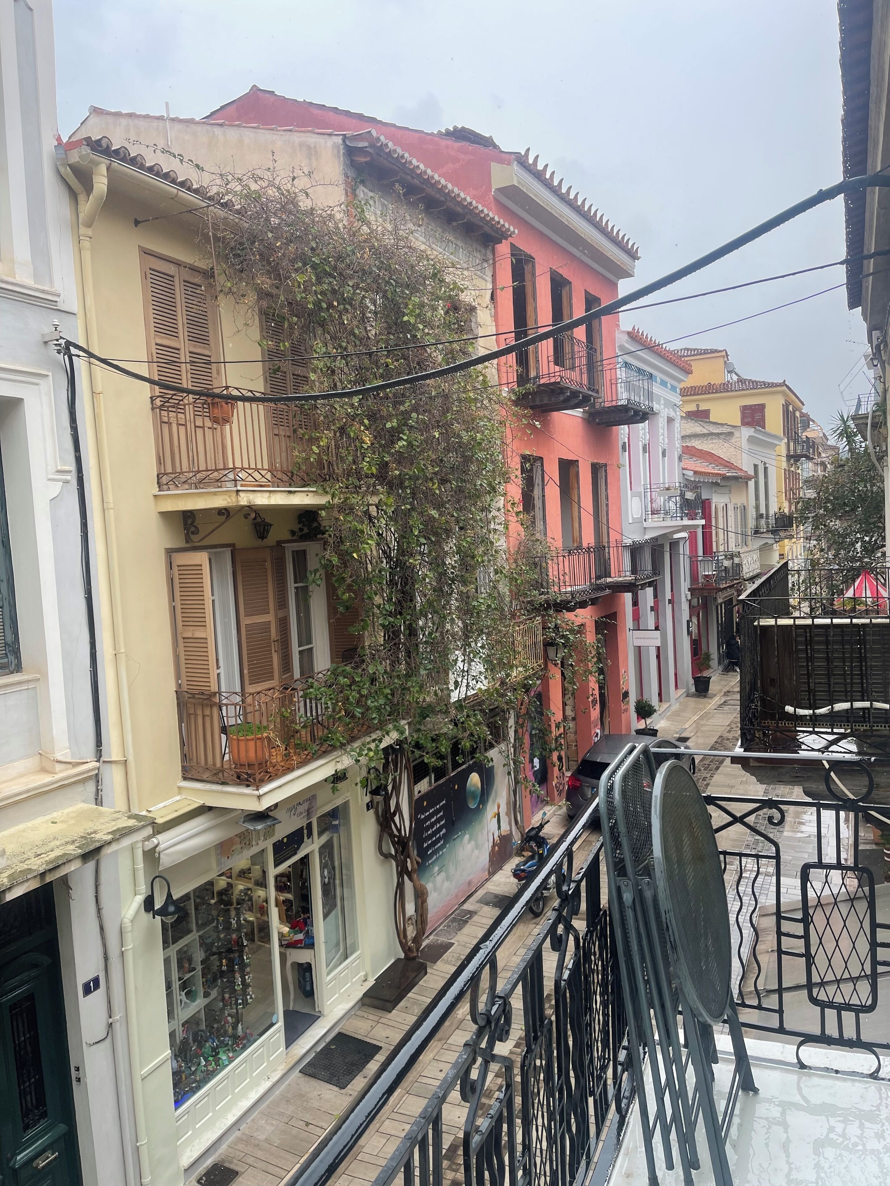 A narrow street with colorful buildings, balconies, and a shop with glass display windows.