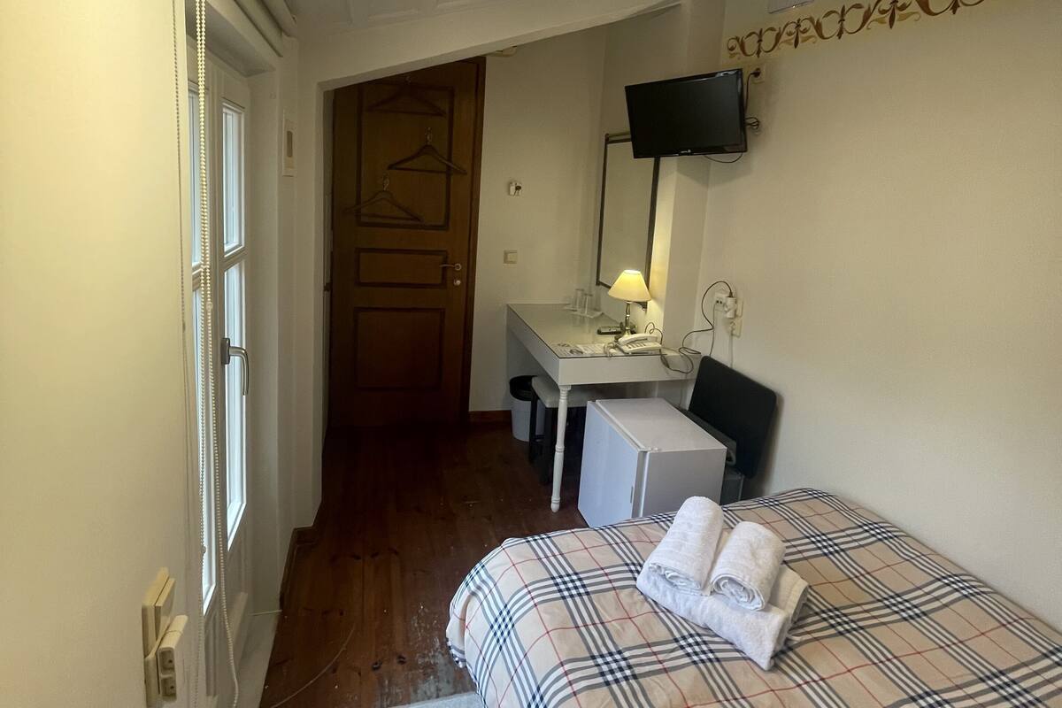 A compact hotel room with a bed, a desk, a chair, a TV, and a wardrobe.