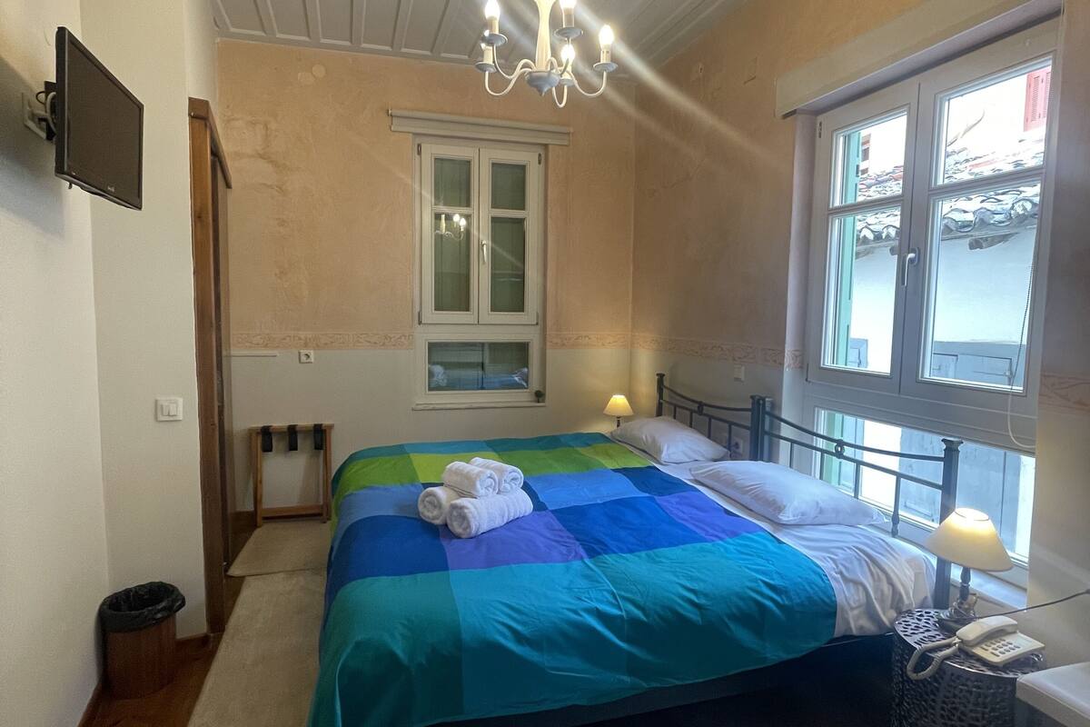 A bedroom with a bed, a chandelier, a window, and a bedside table with a lamp.