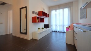 Ein modernes Wohnzimmer mit einem großen Spiegel, einem Fernseher auf einem weißen Schrank und roten Regalelementen.