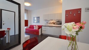 Eine moderne Küche mit weißen Schränken, einer roten Akzentwand und einem Essbereich mit weißem Tisch und roten Stühlen.
