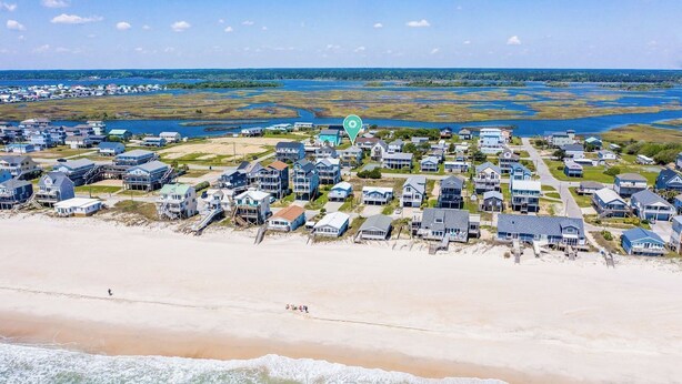 An aerial view of a coastal residential area with houses along the beachfront, a clear sky, and a body of water in the background.