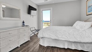 A bedroom with a bed, dresser, ceiling fan, and a door leading to a balcony.