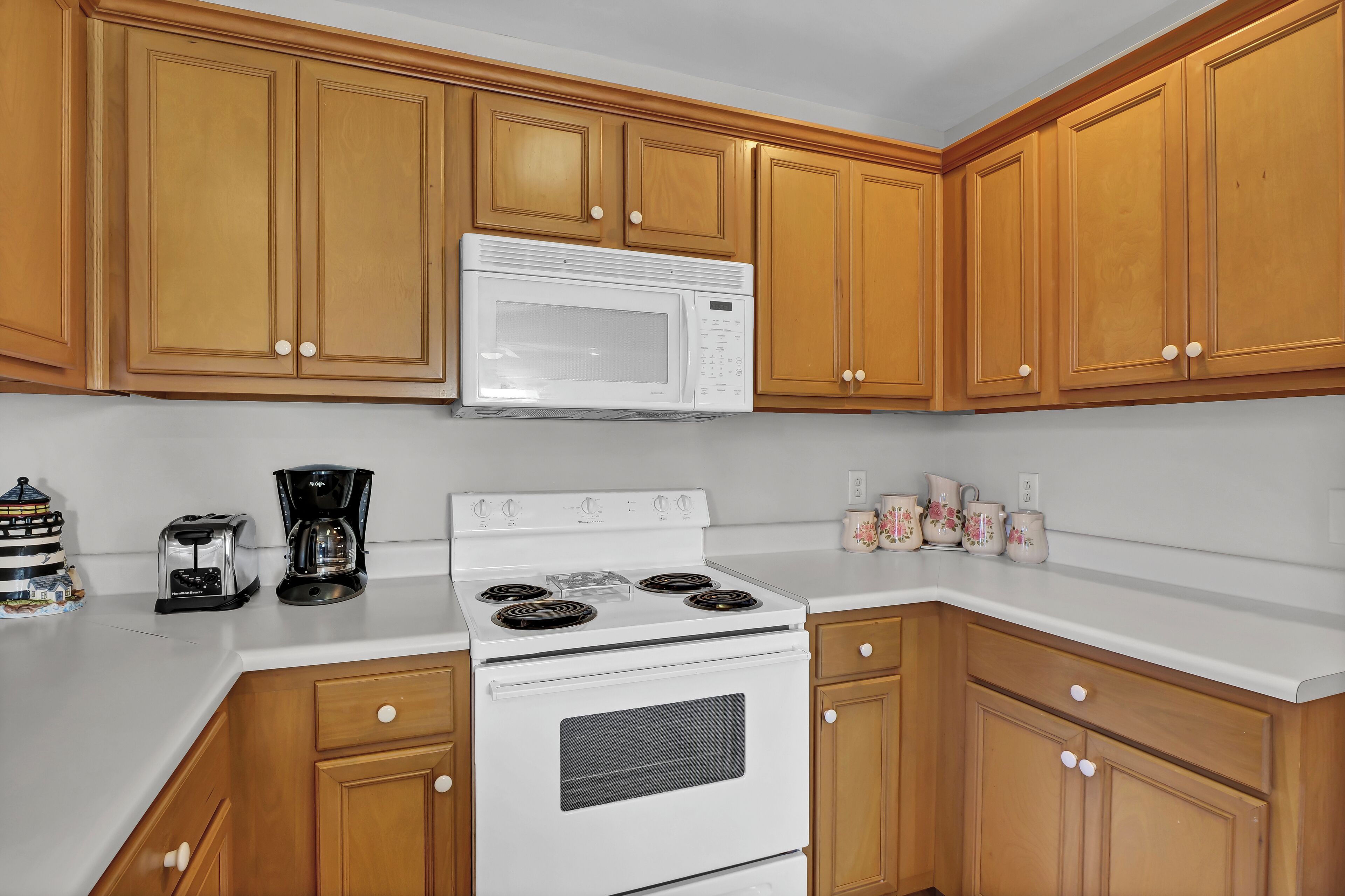 A kitchen with wooden cabinets, a white microwave, a stove, and a coffee maker.