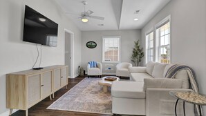 A modern living room with a flat-screen TV, a ceiling fan, a wooden cabinet, a white sofa, and a coffee table.