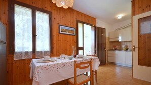 Un coin repas avec une table en bois dressée pour deux personnes, une cuisine en arrière-plan et une porte donnant sur une autre pièce.