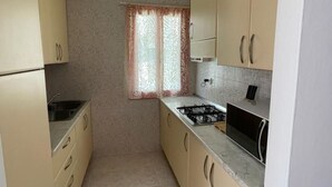 A compact kitchen with beige cabinets, a gas stove, and a window with patterned curtains. - Spacious apartment with terrace in Rosolina Mare (Rosolina Mare)