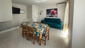 A dining area with a table set for four, a teal sofa, and a ceiling fan. - Spacious apartment with terrace in Rosolina Mare (Rosolina Mare)