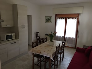 A dining area with a table, chairs, a microwave, and a red sofa.