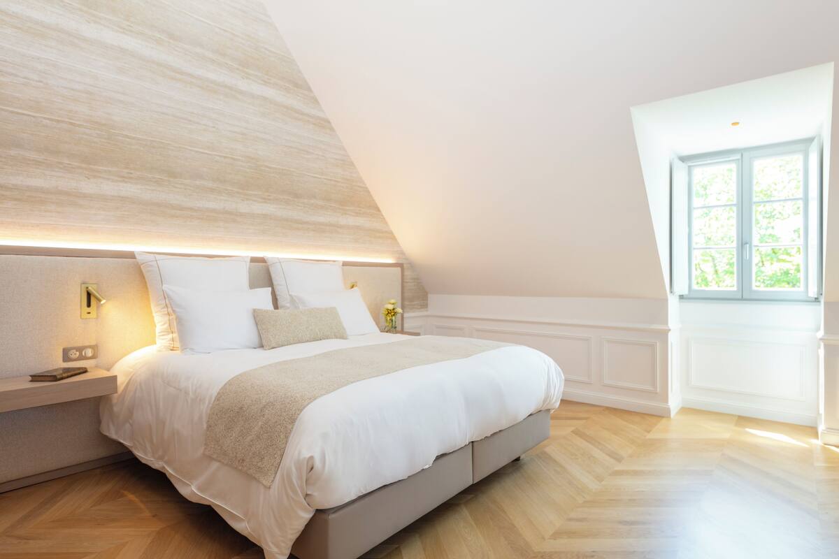 A modern bedroom with a large bed, bedside tables, and a window with a view.