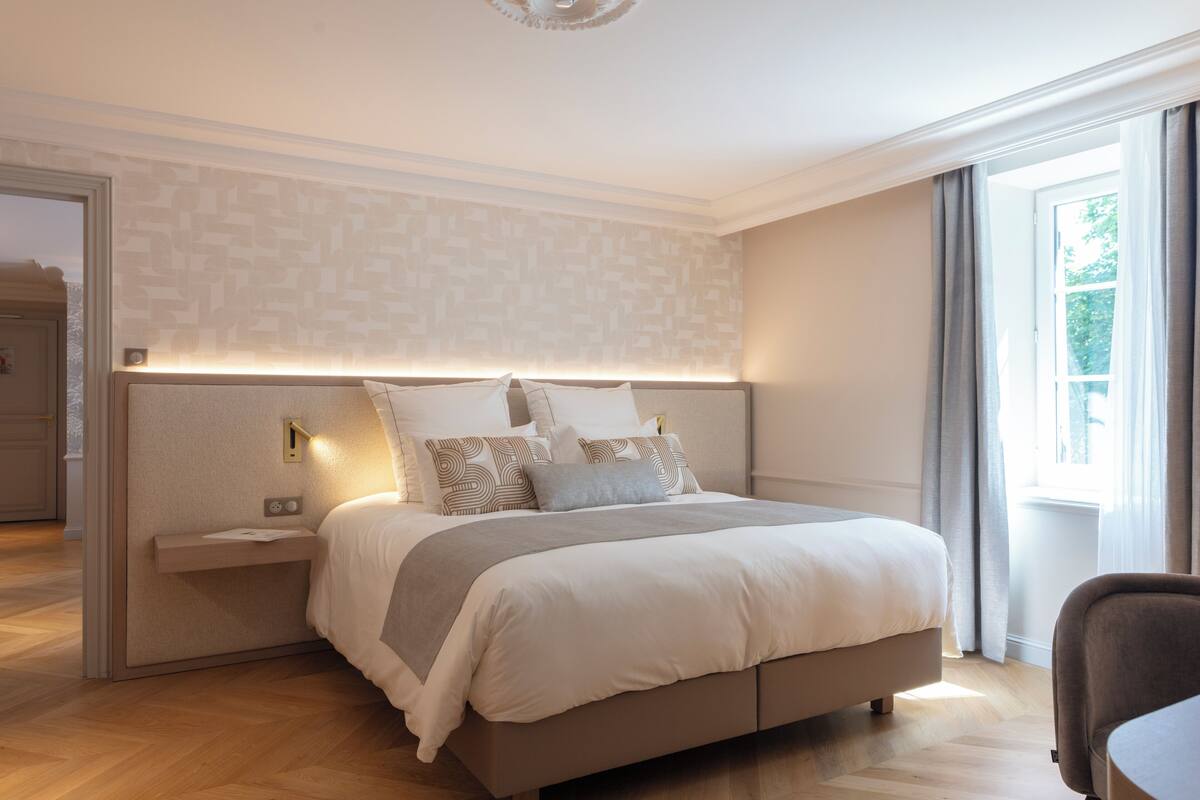 A modern bedroom with a large bed, bedside tables, and a view of the outdoors through a window.
