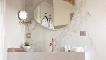 Une salle de bain avec un lavabo en marbre, un robinet doré, un miroir rond et un porte-serviettes.