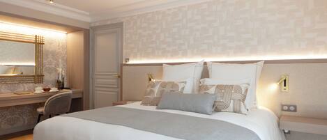 A hotel room with a large bed, bedside tables, a desk, and a mirror.