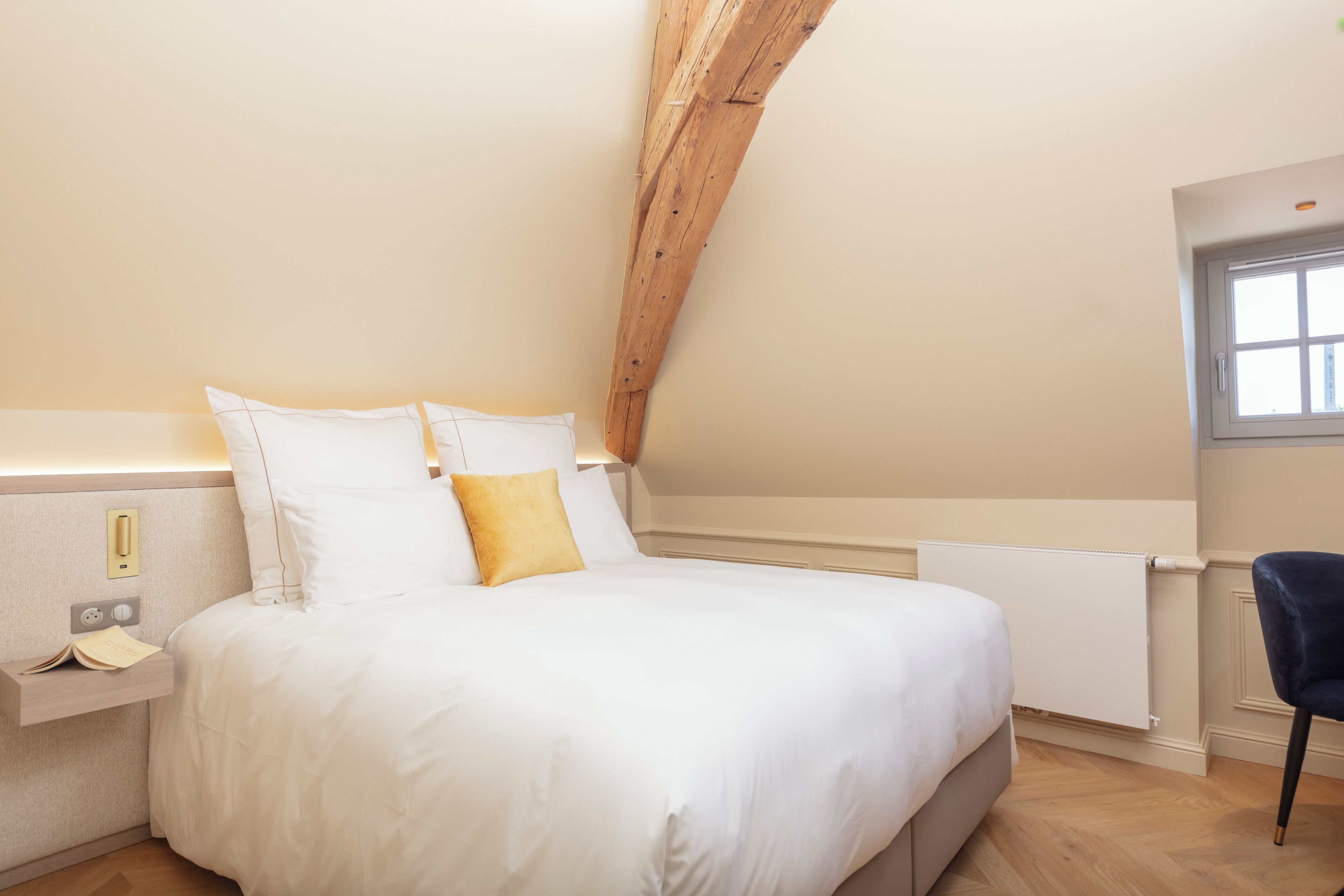 Une chambre avec un lit, une table de chevet, une fenêtre et des poutres en bois au plafond.
