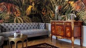 A living room with a grey tufted sofa, a round coffee table with a vase, a wooden cabinet with drawers, and a large tiger mural on the wall. - Le Clos Alice (Arbois)