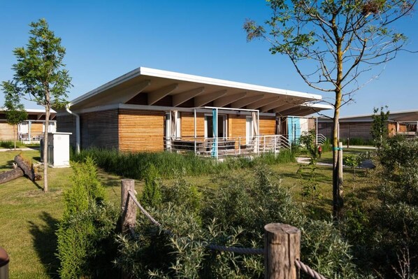 Un bâtiment moderne doté d’un toit plat et d’un revêtement en bois, entouré de verdure et surplombé d’un ciel dégagé.