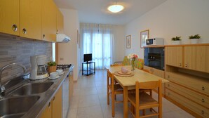 A modern kitchen with stainless steel appliances, wooden cabinets, and a dining area with a table and chairs. - Shining flat in Bibione - Beahost (Bibione)
