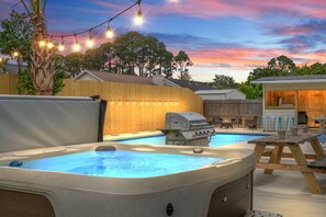 Un jardin avec un jacuzzi, un barbecue et une terrasse en bois.
