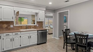 Una cocina moderna con armarios blancos, lavavajillas y comedor con una mesa para cuatro.