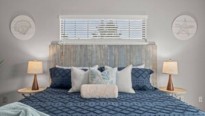 Un dormitorio con una cama grande, dos mesitas de noche, cabecera y decoración en la pared.