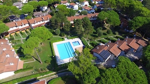 Vue aérienne d’un quartier résidentiel avec une piscine entourée d’arbres et de maisons.