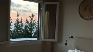 Un dormitorio con cama, ventana con vistas a árboles, techo de madera y una lámpara fijada a la pared.