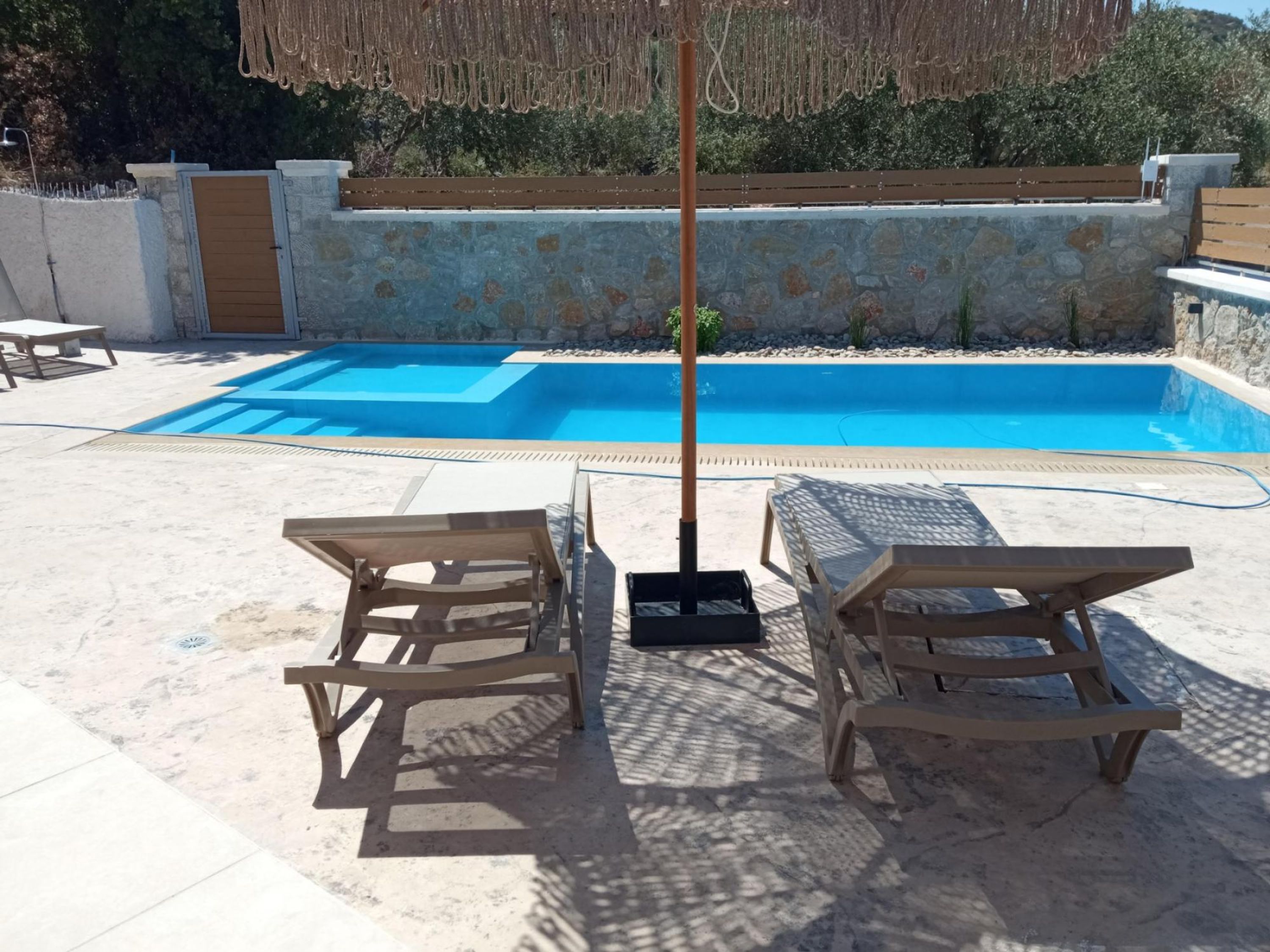 Une piscine avec deux chaises longues en bois et un parasol en chaume.
