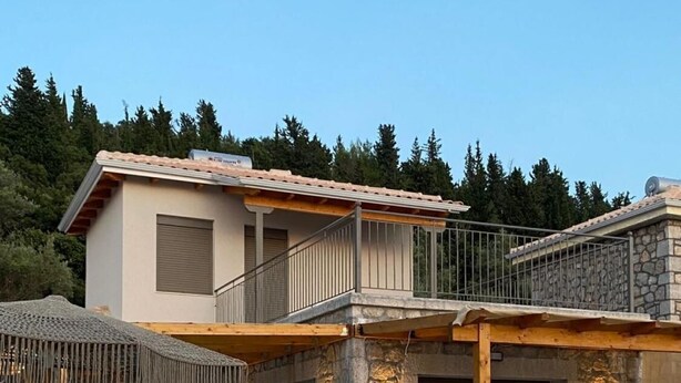 Una casa de dos pisos con fachada de piedra, un balcón y una zona de estar al aire libre cubierta con sillones de descanso.