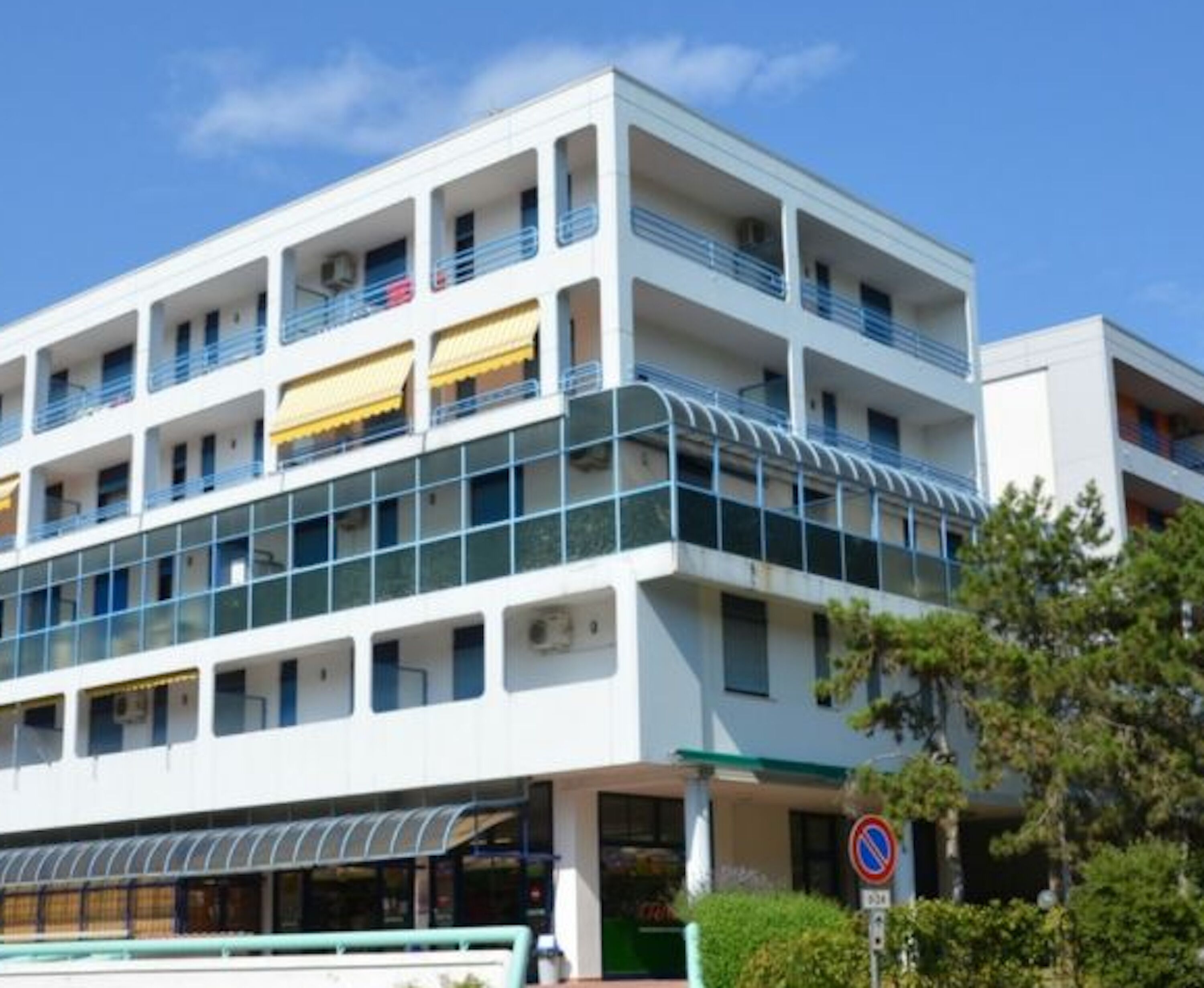 A multi-story building with balconies, large windows, and a no parking sign.