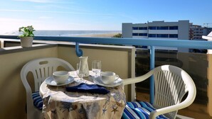 A balcony with a table set for two, overlooking a beach and buildings. - Enjoyable house that overlooks the sea (Bibione)