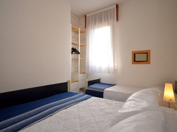 A hotel room with two beds, a wardrobe, and a window with curtains.