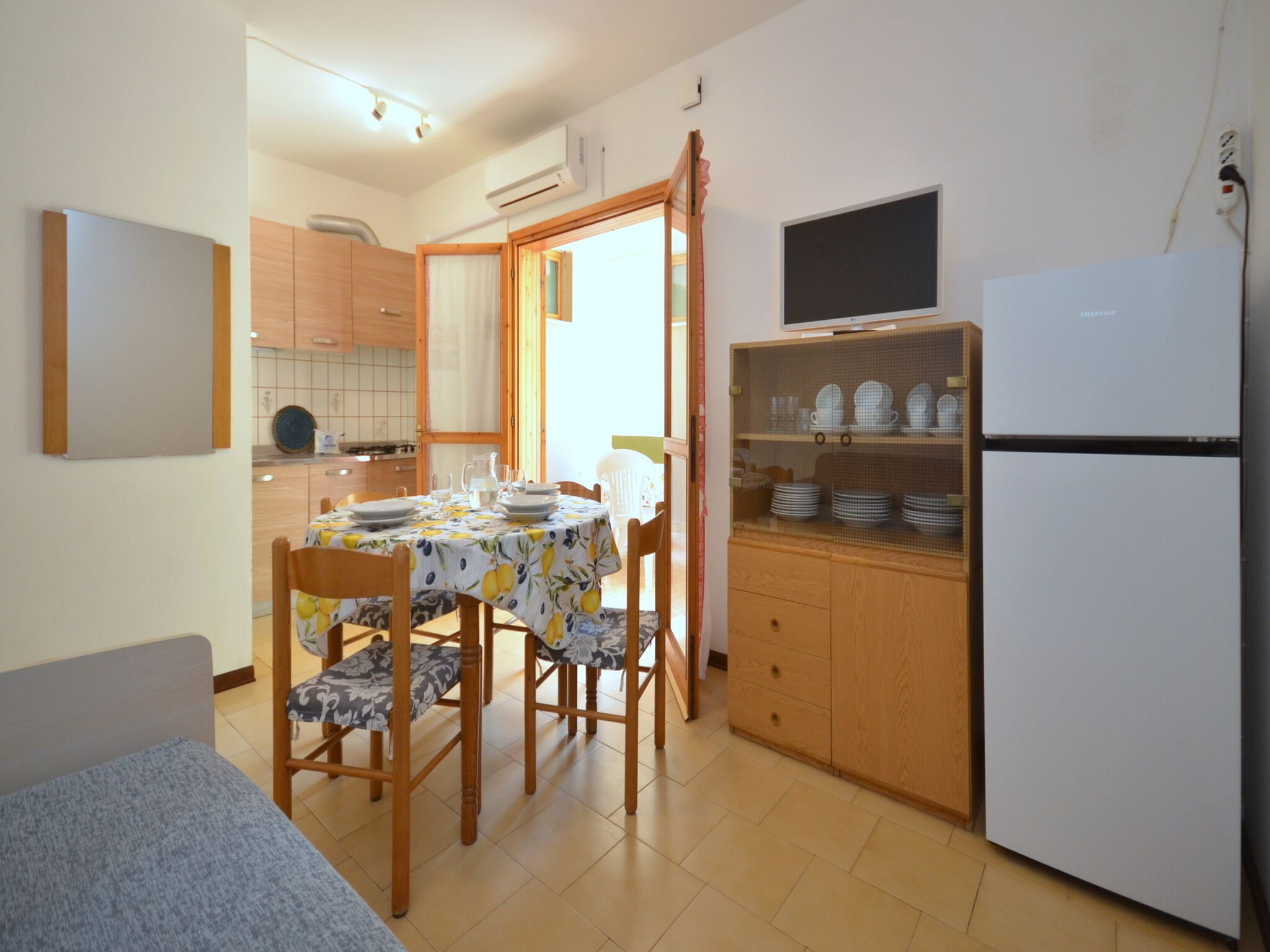 A compact kitchen with a dining table, chairs, a refrigerator, and a cabinet with dishes.