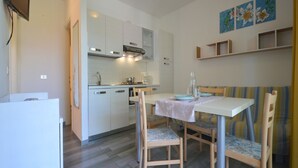 Une cuisine de taille réduite avec des meubles blancs, une table à manger avec des chaises et un téléviseur fixé au mur.