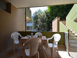 A balcony with a table and chairs, a staircase, and a view of trees and buildings. - Adorable modern holiday flat (Bibione)