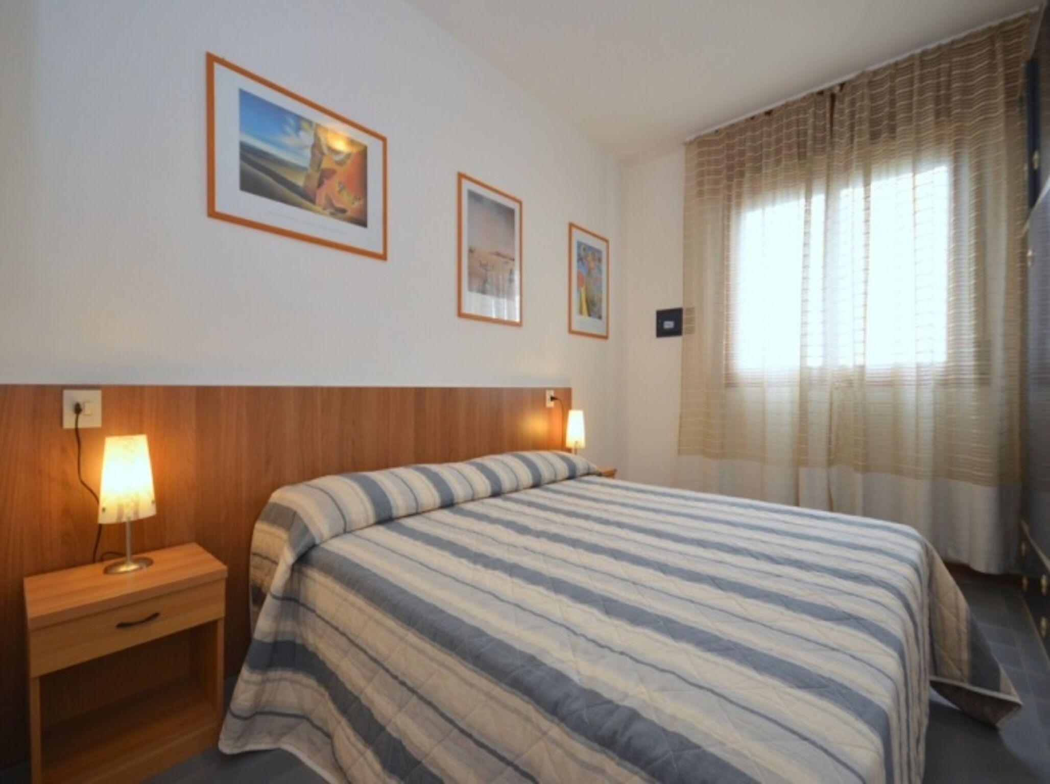 Une chambre d’hôtel avec un lit, une table de chevet, une lampe et deux tableaux encadrés au mur.