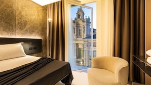 A hotel room with a large bed, a chair, and a view of a historic building through a glass door. - Meo Design Suite & Spa (Catania)