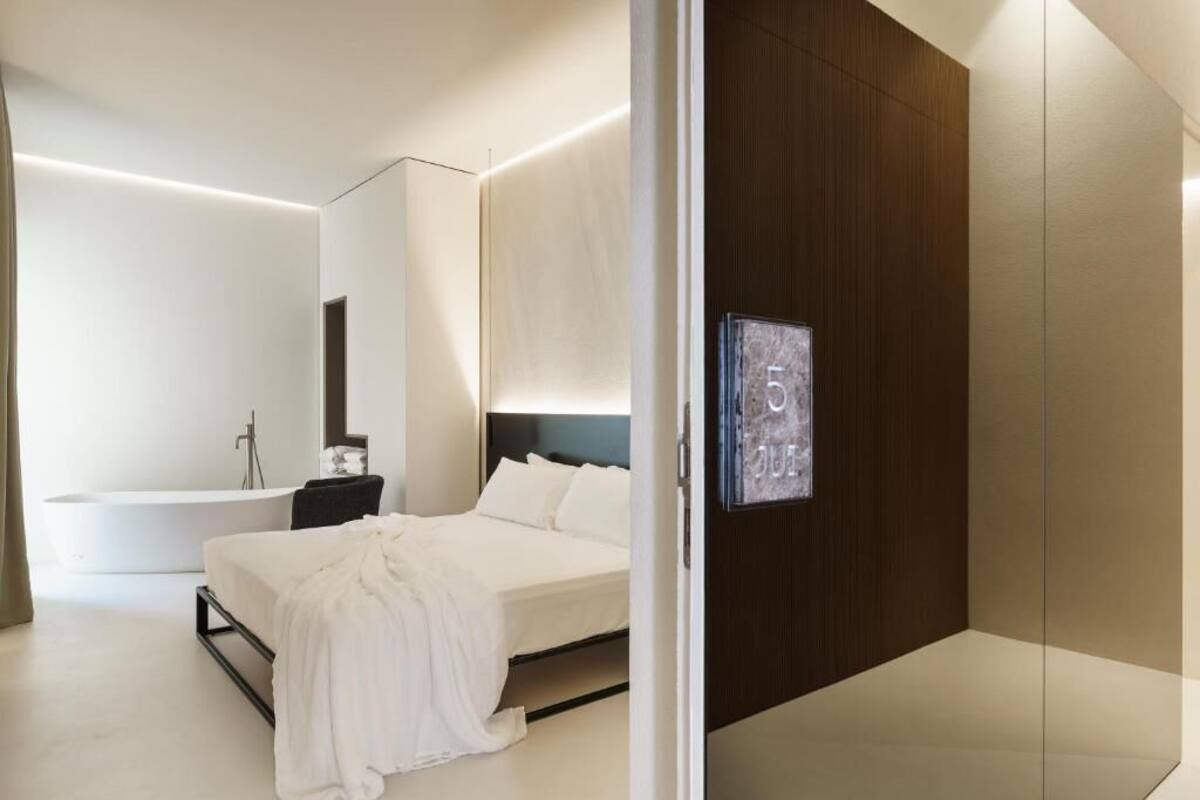A modern bedroom with a large bed, a built-in TV, and a separate bathroom with a bathtub.