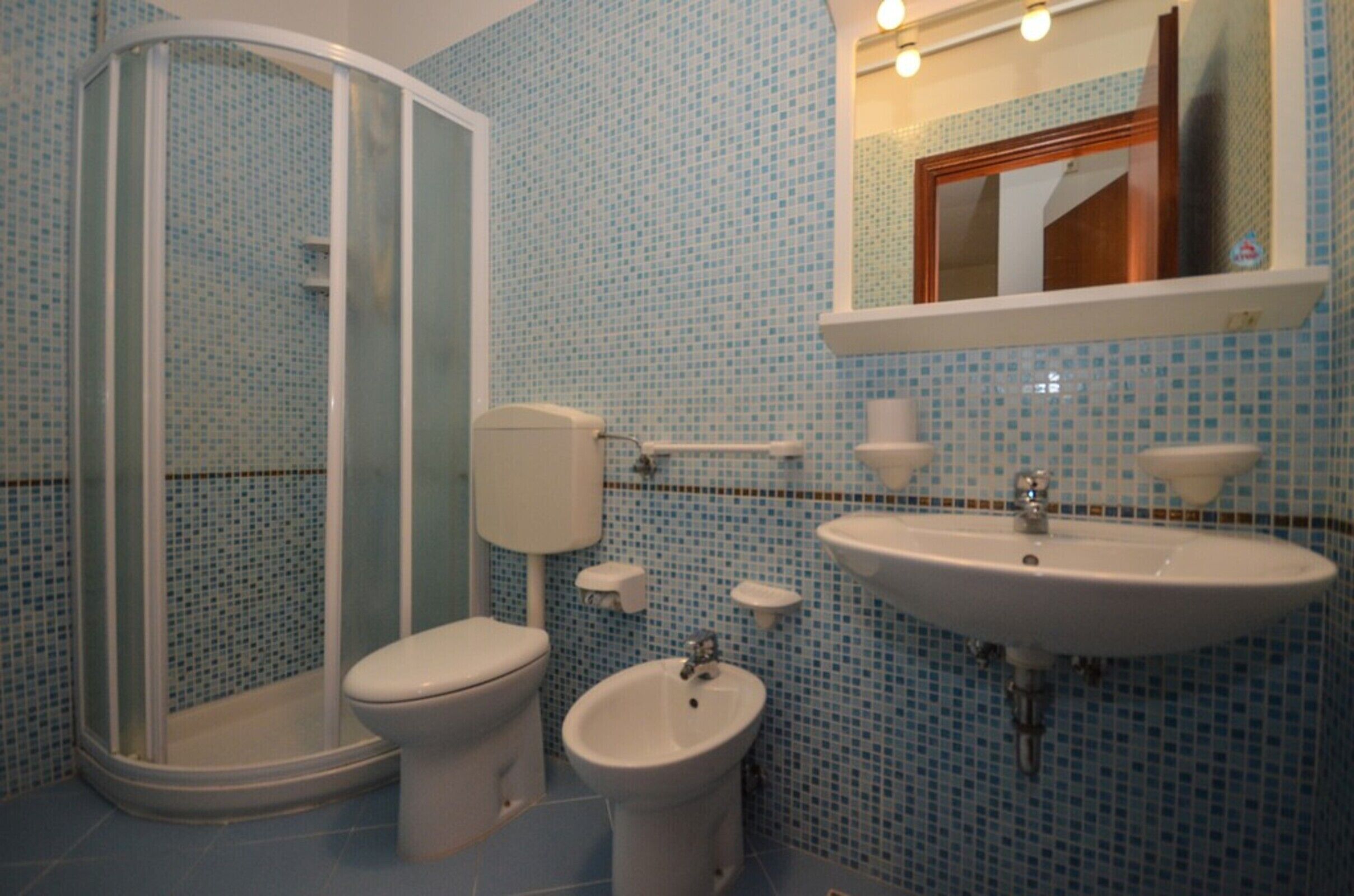 A bathroom with a shower, toilet, bidet, and sink.