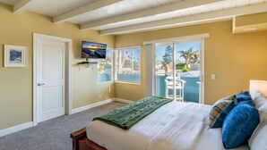 A bedroom with a bed, a television, a door, and a window with blinds. - Summer Sunset - Easy Breezy Beach Life in Ventura (Ventura)