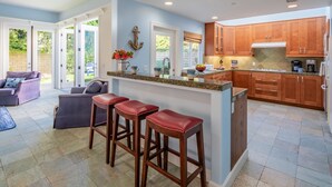 A modern kitchen with wooden cabinets, a granite countertop, and a built-in island with stools. - Summer Sunset - Easy Breezy Beach Life in Ventura (Ventura)
