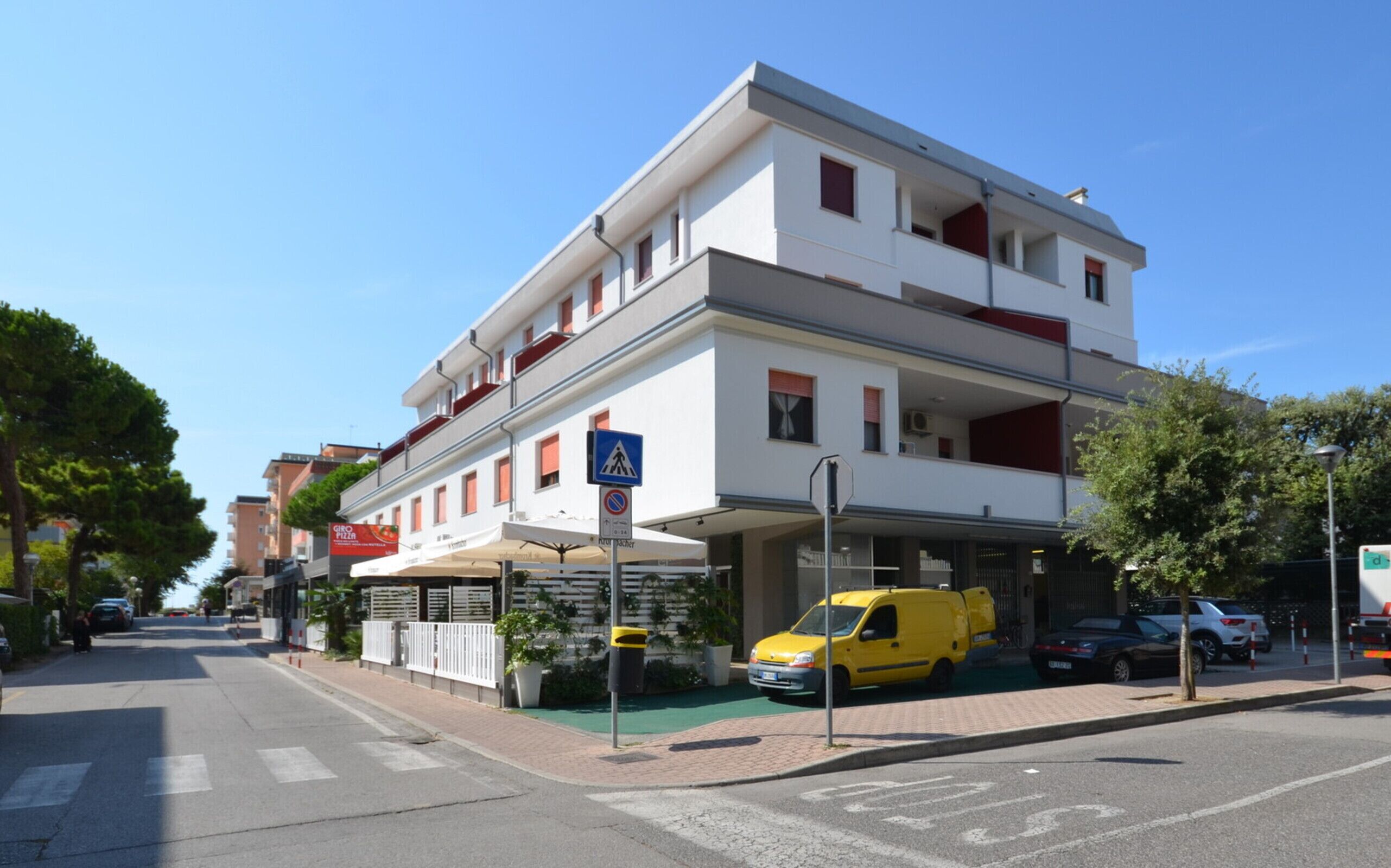 A multi-story building with a white facade, a pedestrian crossing sign, and a yellow van parked in front.